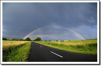 Picture of a rainbow at the end of a road.